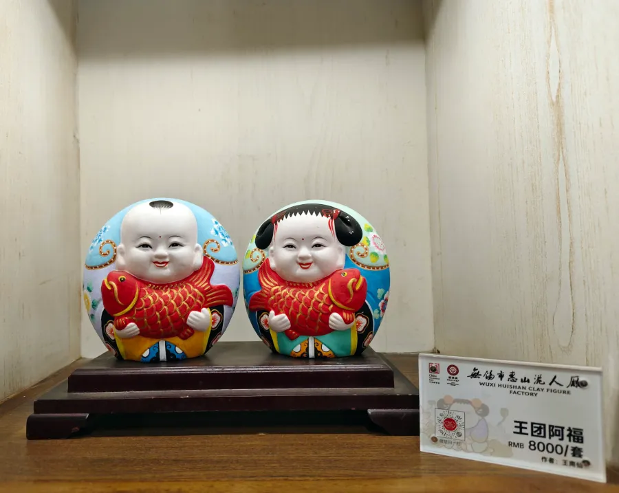 A colorful pair of smiling Da A Fu clay figurines displayed on a wooden stand.