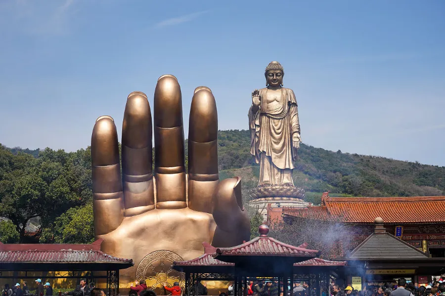 The giant bronze Lingshan Buddha statue stands on a green hill under a clear sky.